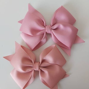 May include: Two pink satin hair bows with a simple design. The bows are tied together in the centre with a small piece of ribbon.