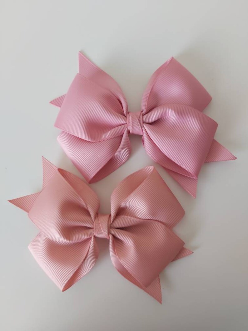 May include: Two pink satin hair bows with a simple design. The bows are tied together in the centre with a small piece of ribbon.