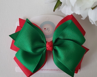 May include: A green and red double bow hair clip. The bow is made of grosgrain ribbon and is attached to a clip. The clip is labeled "AG Handmade Designs."