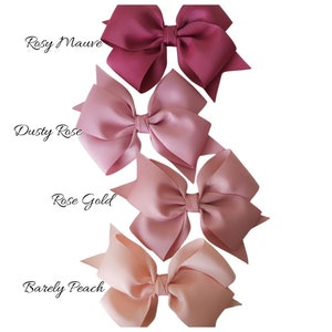 May include: Four hair bows in shades of pink, from dark to light: Rosy Mauve, Dusty Rose, Rose Gold, and Barely Peach.