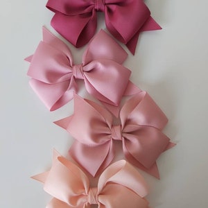 May include: Four hair bows in shades of pink, from dark pink to light peach. The bows are made of satin ribbon and are tied in a classic bow shape.