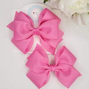 May include: Two pink hair bows with a white card behind them. The card has the text "AG Handmade Designs" on it.