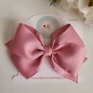 May include: A large pink satin bow with a white card that says "AG Handmade Designs" and "www.shopagandmade designs.com".