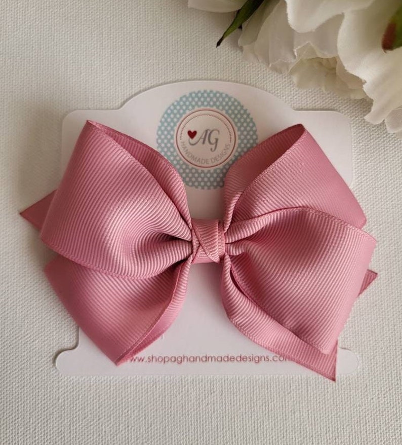 May include: A large pink satin bow with a white card that says "AG Handmade Designs" and "www.shopagandmade designs.com".