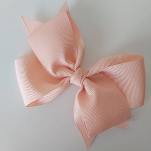 May include: A peach-coloured hair bow with a large, double-looped bow. The bow is made of a soft, textured fabric.