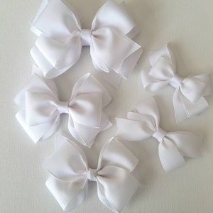 May include: Five white satin ribbon bows of varying sizes. The bows are arranged on a white surface.