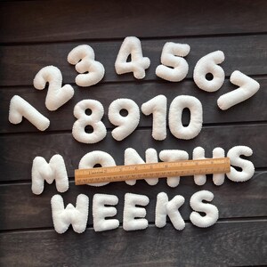 May include: White felt numbers 1 through 10 and the words "MONTHS" and "WEEKS" on a dark wood background.