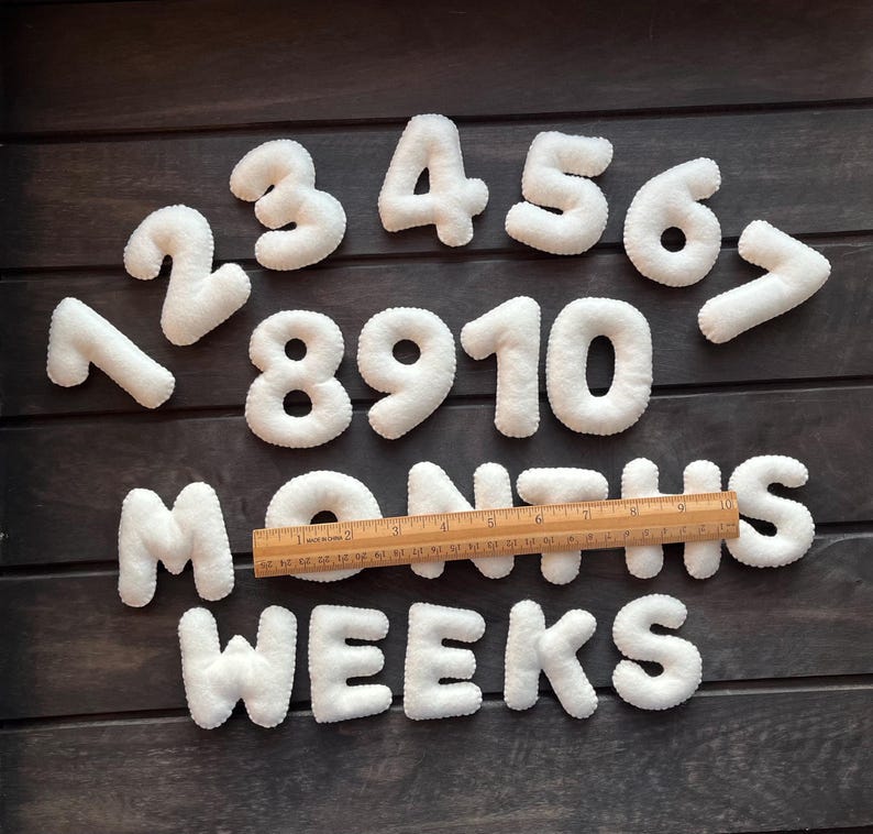 May include: White felt numbers 1 through 10 and the words "MONTHS" and "WEEKS" on a dark wood background.