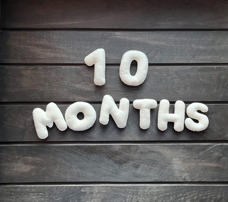 May include: White felt letters spelling out "10 months" on a dark wood background.