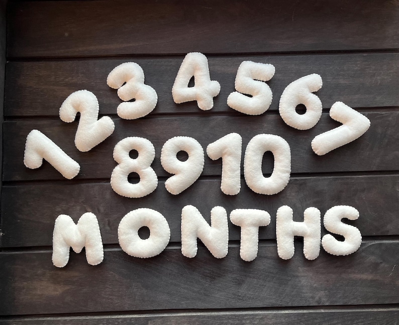 May include: White felt numbers 1 through 10 and the word "MONTHS" on a dark brown wooden background.