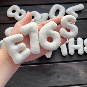 May include: White felt letters spelling out the number "168" in a hand. The letters are thick and have a slightly puffy appearance.