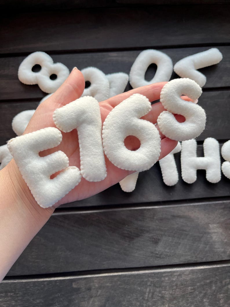 May include: White felt letters spelling out the number "168" in a hand. The letters are thick and have a slightly puffy appearance.