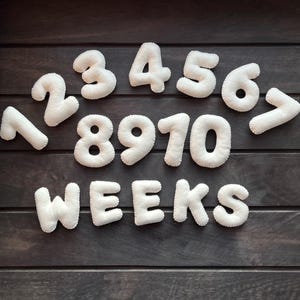 May include: White felt numbers 1 through 10 and the word "WEEKS" arranged in a semi-circle on a dark wood background.