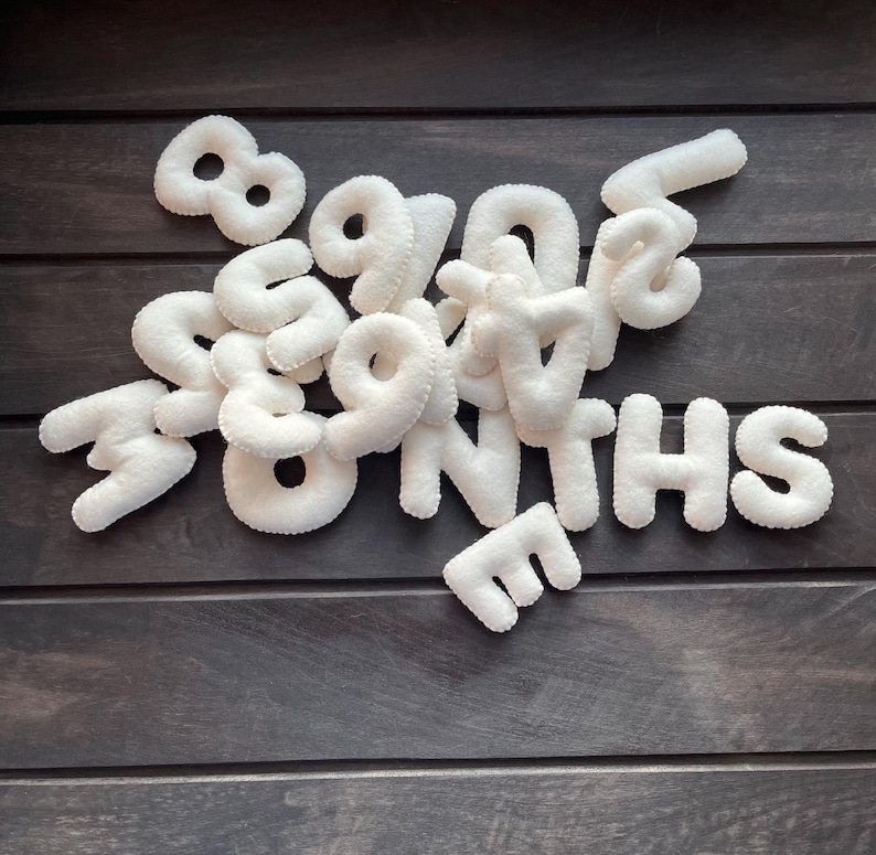 May include: White felt letters spelling out "MONTHS" for a baby milestone photo prop.