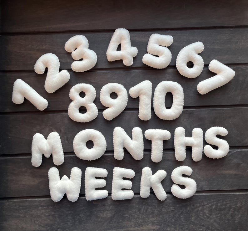 May include: White felt numbers 1 through 10, along with the words "MONTHS" and "WEEKS", arranged on a dark wood background.