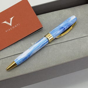 May include: A blue and white marbled pen with gold accents and the Visconti logo on the side, in a grey box with a red card that says Visconti.
