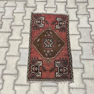 May include: A red and brown patterned rug with a geometric design. The rug has a fringe border and is made of wool.