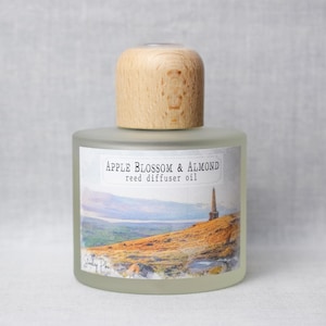 May include: Frosted glass reed diffuser bottle with a wooden cap. The label reads "Apple Blossom & Almond reed diffuser oil" with a landscape illustration. The bottle is designed for home fragrance.