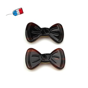 以下が含まれることがあります： 茶色と黒のプラスチック製の蝶ネクタイ型のヘアクリップが2つ。