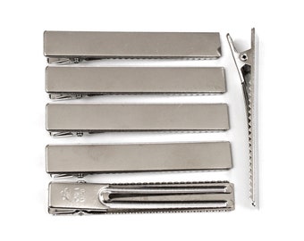 May include: Six silver metal hair clips, each with a textured surface and a serrated edge. The clips are arranged in a row, with the largest clip at the bottom and the smallest clip at the top.