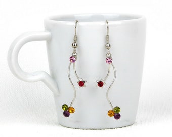 May include: A pair of silver dangle earrings with a wavy design. The earrings feature multiple colorful crystals, including red, pink, green, and purple.