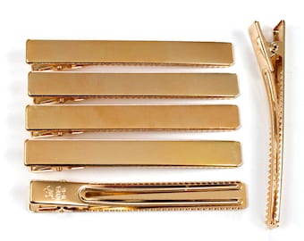 May include: Set of six gold metal hair clips. The clips are rectangular and have a textured surface. One clip is shown open.