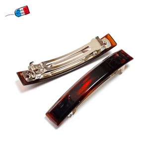 May include: Two rectangular hair barrettes with a tortoiseshell pattern in shades of brown and red. The barrettes have a silver metal clasp. The image includes a small flag that says "Made in France."