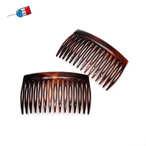 May include: Two brown tortoiseshell hair combs with curved tops and long, thin teeth. The combs are made of a glossy material and are set against a white background. A small tag that says "Made in France" is in the upper left corner.