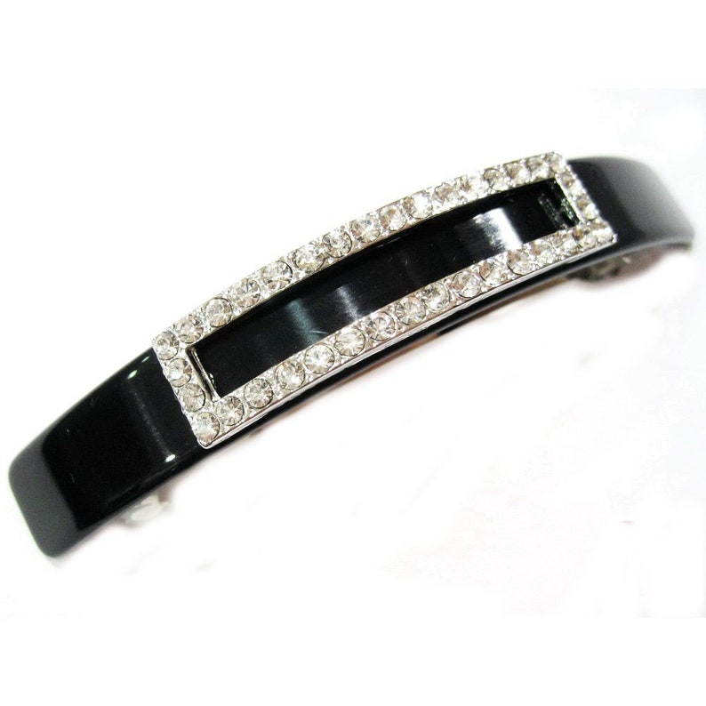 Puede incluir: Pinza para el pelo de pl&aacute;stico negro con un marco rectangular de diamantes de imitaci&oacute;n.