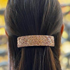 May include: A rose gold glitter hair clip. The clip is rectangular and has a smooth, shiny finish.