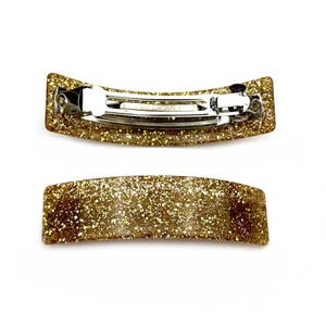 May include: Two gold glitter hair clips. The top clip has a silver metal clasp. The bottom clip is plain.