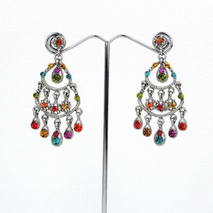 Puede incluir: Un par de pendientes colgantes de plata con detalles de cristal de colores. Los pendientes tienen forma de lágrima con varios niveles de cristales.