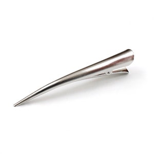 Peut inclure: Une pince &agrave; cheveux en m&eacute;tal argent&eacute; au design long, fin et effil&eacute;. L'accessoire pr&eacute;sente une finition lisse et polie ainsi qu'un m&eacute;canisme &agrave; charni&egrave;re &agrave; l'extr&eacute;mit&eacute; la plus large, permettant de l'ouvrir et de le fermer pour maintenir les cheveux.