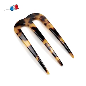 Peut inclure: Une fourche à cheveux à trois dents avec un motif écaille de tortue. L'accessoire pour cheveux est fait d'un matériau brillant avec des nuances de marron, de noir et de jaune. L'étiquette sur l'image indique "Made in France".
