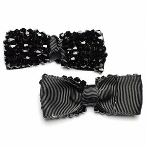 以下が含まれることがあります： 黒いヘアクリップが2つ。1つは黒いリボンボウ、もう1つは黒いクリスタルビーズが付いている。