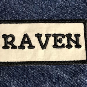 May include: White patch with black stitching and the word "RAVEN" embroidered in black.