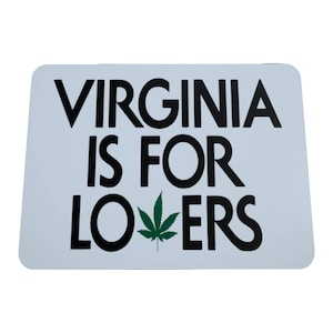 May include: A white rectangular sign with rounded corners. The sign features the text "VIRGINIA IS FOR LOVERS" in bold black letters. A green cannabis leaf replaces the "O" in "LOVERS".