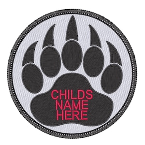May include: A white and gray embroidered patch with a black bear paw print. The paw print has five toes and claws. The text "CHILDS NAME HERE" is embroidered in red in the center of the paw print.