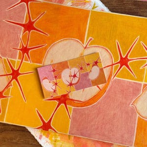 以下が含まれることがあります： オレンジ、黄色、ピンクの鮮やかな色使いの抽象的なアートワーク。デザインには、リンゴの形、スターバースト、幾何学模様が含まれています。同様のデザインの小さなカードが上に置かれています。アーティストの名前「brookleebee」が下にあります。