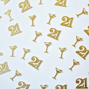 May include: Gold glitter confetti featuring the number "21" and martini glasses. The scattered shapes are on a white background. This festive confetti is suitable for a 21st birthday celebration or party.