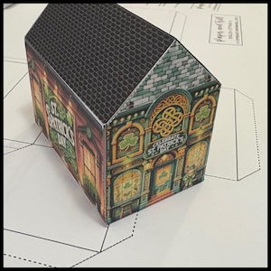 May include: A papercraft model of a green and gold building with a black roof. The building has a sign that says "Celebrate St. Patrick's Day".