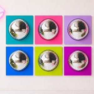 May include: Six square wall art panels, each featuring a centered silver disco ball. The panels are colored in teal, hot pink, light purple, royal blue, lime green, and magenta. A neon pink lip-shaped light is visible on the upper left side.