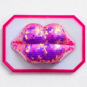 May include: A pink and purple mosaic lips art piece. The lips are framed in a bright pink, octagonal border, set against a white background. The lips are made of small, reflective squares, creating a disco ball effect.