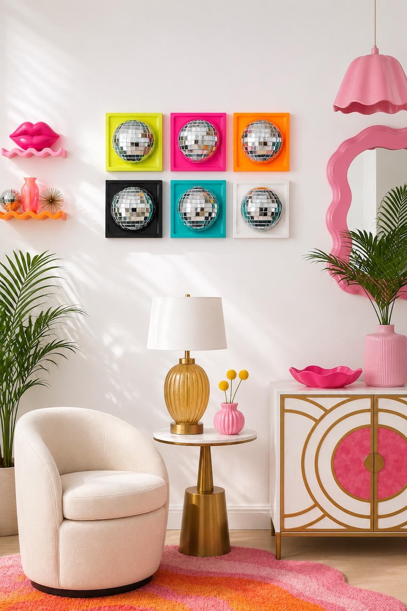 May include: A wall display featuring six square frames with mirrored disco balls, a pink lip sculpture, two wavy shelves, a cream armchair, a gold lamp with a white shade, a pink vase, and a white cabinet with gold geometric accents.