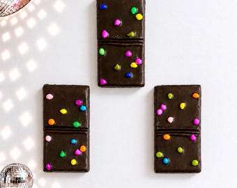 May include: Three rectangular dark brown domino-shaped wall decorations, each featuring a horizontal line dividing the piece into two squares. The surfaces are decorated with small, colorful, round candy-like accents in pink, blue, green, yellow, and orange.