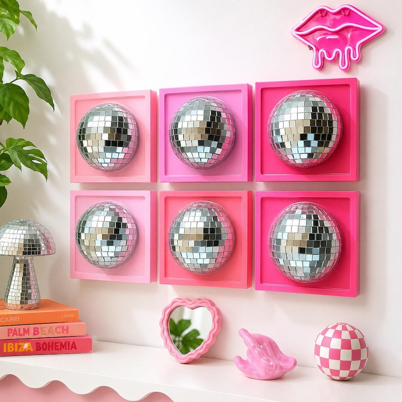 May include: Six square wall-mounted frames in varying shades of pink, each containing a silver mirrored disco ball sphere. A neon pink lip-shaped light, a mushroom-shaped disco ball, a heart-shaped mirror, a pink sculpture, and a checkered ball.