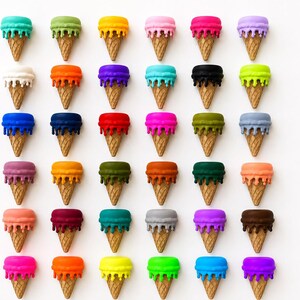 May include: A grid of thirty-six miniature ice cream cone sculptures arranged in six rows and six columns. Each cone features a textured tan base topped with a smooth, solid-colored scoop of ice cream that appears to be melting down the sides.