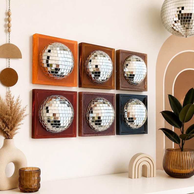 May include: Six square wall art pieces, each featuring a centered, silver mirrored disco ball hemisphere. The frames are colored in shades of orange, light brown, dark brown, deep red, maroon, and black, arranged in two rows of three on a wall.