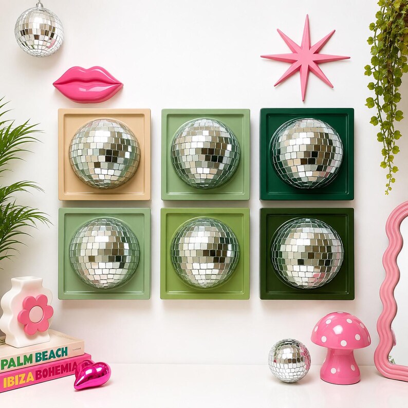 May include: Six square wall-mounted frames in beige, light green, olive green, and dark green, each containing a reflective silver disco ball sphere. The display includes a pink lip-shaped wall decor, a pink star, and a pink mushroom lamp.