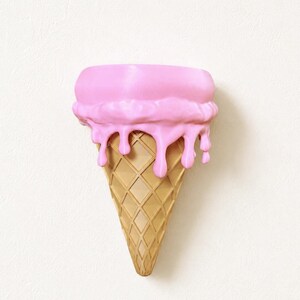 May include: A wall-mounted ice cream cone sculpture featuring a tan, diamond-patterned waffle cone base topped with a thick layer of smooth, bright pink ice cream that appears to be melting down the sides of the cone in rounded drips.